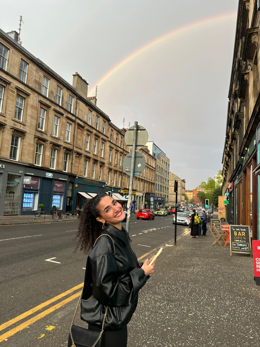 Joy smiling on a city street under a rainbow